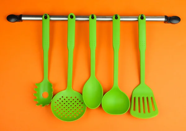 Plastic kitchen utensils on silver hooks on orange background — Stock Photo, Image