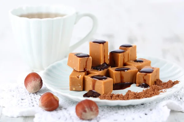 Many toffee on plate and cup of tea on napkin on wooden table — Stock Photo, Image