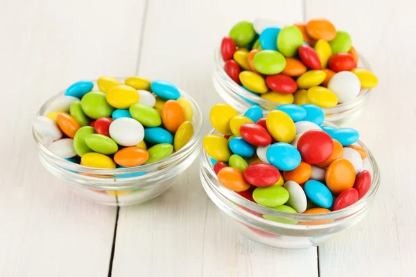 Coloridos caramelos en cuencos de vidrio sobre fondo blanco de madera —  Fotos de Stock