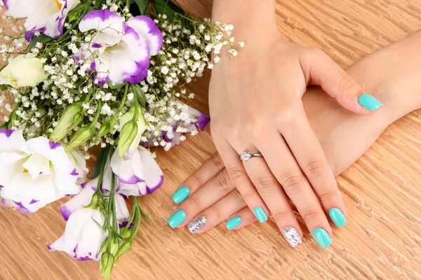 Beautiful woman hands with blue manicure near bouquet of beautiful flowers, on color background — Stock Photo, Image