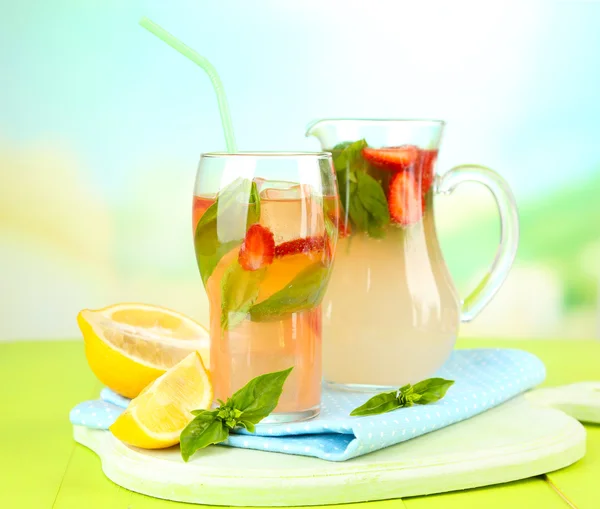 Basil limonade met aardbei in kruik en glas, op houten tafel, op lichte achtergrond — Stockfoto