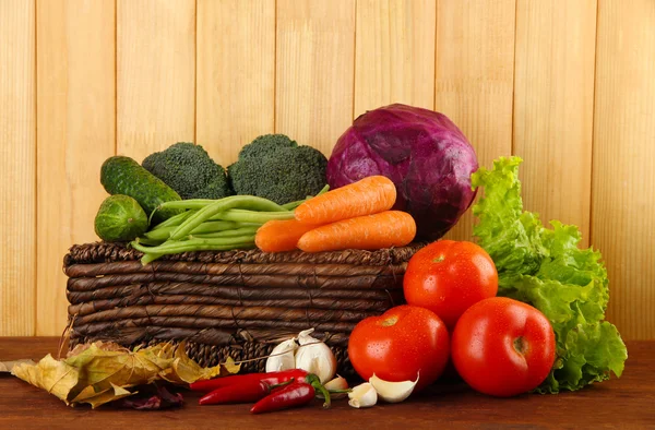 Différents légumes sur panier avec des feuilles jaunes sur table sur fond en bois — Photo