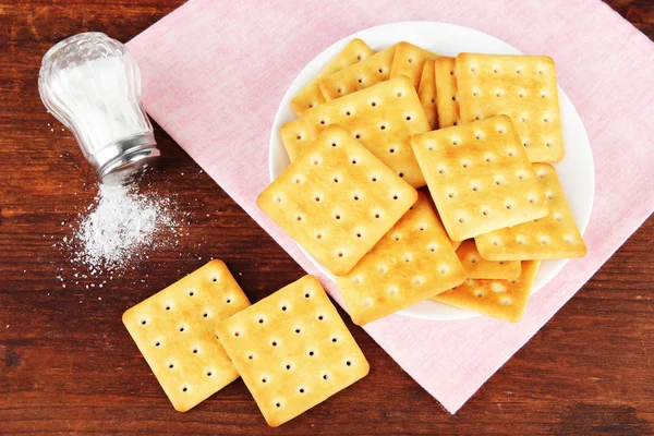 Leckere Cracker mit Salz und Serviette auf Holzgrund — Stockfoto