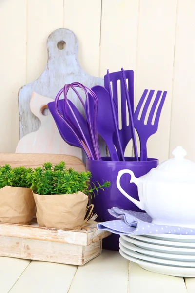 Plastic kitchen utensils in cup on wooden table — Stock Photo, Image