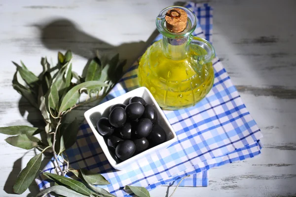 Оливки в миске с веткой на мешковине на деревянной доске на столе — стоковое фото