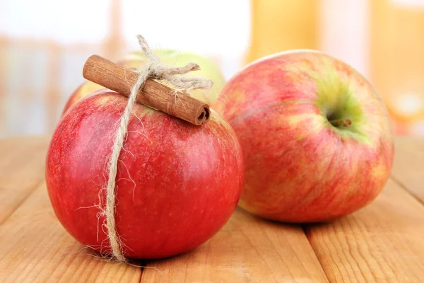 Manzanas maduras con palitos de canela sobre mesa de madera, sobre fondo brillante — Foto de Stock