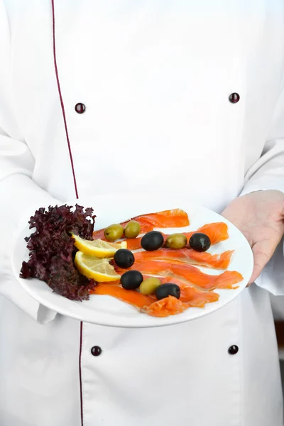 Fisch auf dem Teller in der Hand des Kochs auf hellem Hintergrund — Stockfoto