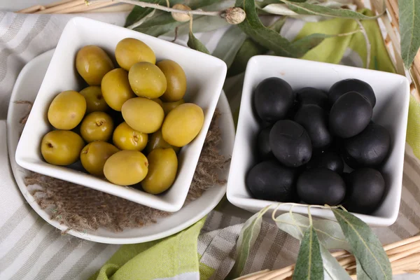 Оливки в мисках с веткой на салфетке в корзине крупным планом — стоковое фото