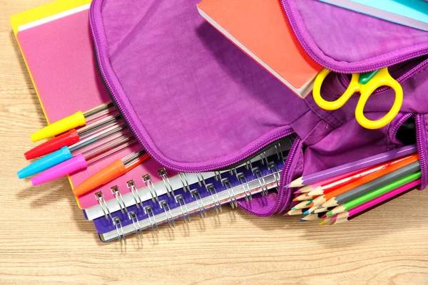 Sac à dos violet avec fournitures scolaires sur fond en bois — Photo