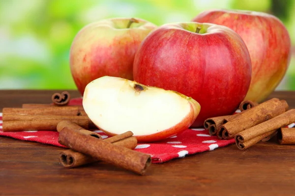Ripe apples with with cinnamon sticks on wooden table, on bright background — Stock Photo, Image
