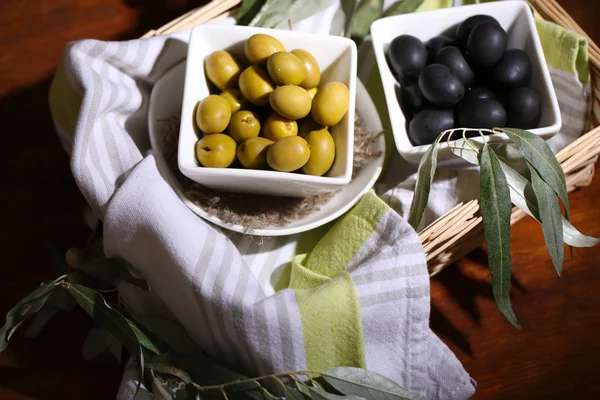 Aceitunas en cuencos con rama en servilleta en cesta sobre mesa de madera —  Fotos de Stock