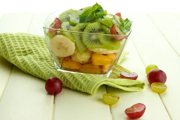 Smakelijke fruitsalade in glazen kom, op witte houten tafel — Stockfoto