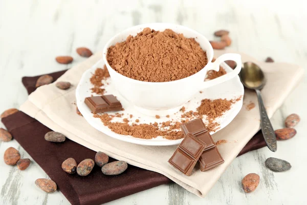 Cocoa powder in cup on napkin on wooden table — Stock Photo, Image