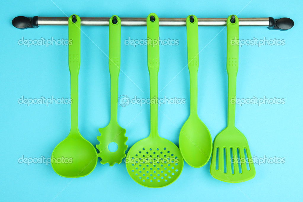 Plastic kitchen utensils on silver hooks on blue background — Stock