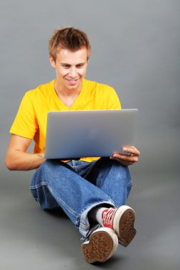 un joven guapo con portátil sobre fondo gris