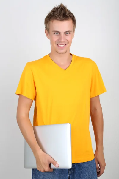 Un joven guapo con portátil sobre fondo gris — Foto de Stock