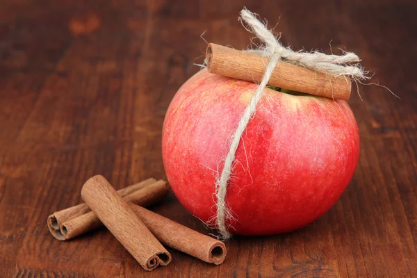 Ripe apples with with cinnamon sticks on wooden background — Stock Photo, Image