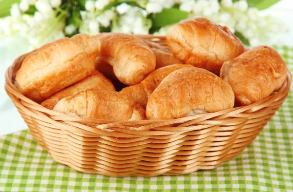 Chutné croissanty v proutěném koši na stole na bílém pozadí — Stock fotografie