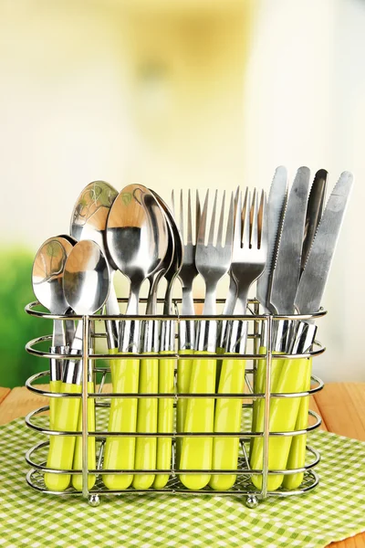 Cuchillos, tenedores y cucharas en soporte de metal sobre mesa sobre fondo brillante — Foto de Stock