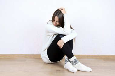 Sad woman sitting on floor near wall clipart
