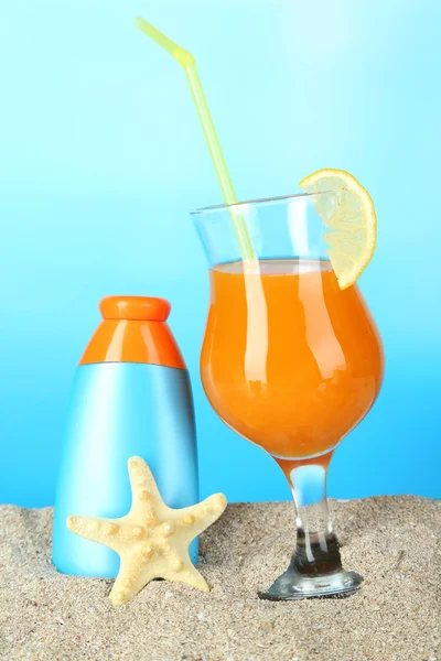 Strand cocktail en zonnebrandcrème in zand op blauwe achtergrond — Stockfoto