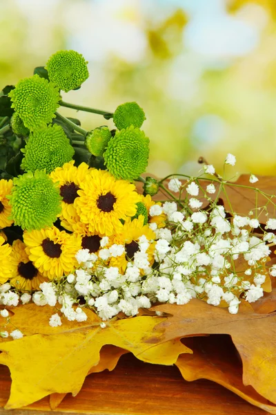 Beautiful flowers with yellow leaves on table on bright background — Stock Photo, Image