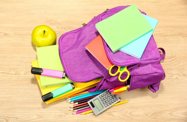 Purple backpack with school supplies on wooden background — Stock Photo, Image