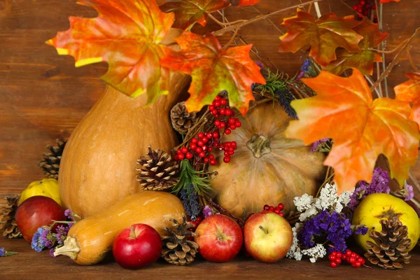 Autumn composition of apples, pumpkins, flowers and dry branches on wooden table on wooden background — Stock Photo, Image