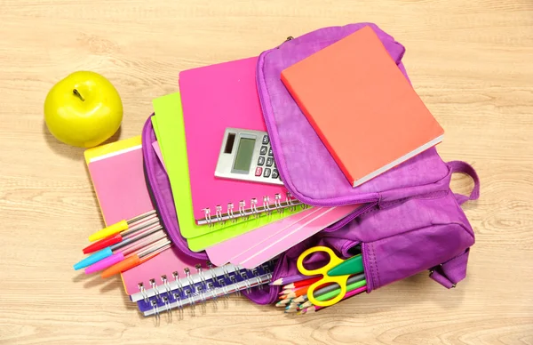 Ahşap arka plan üzerinde mor sırt çantası ile okul malzemeleri — Stok fotoğraf