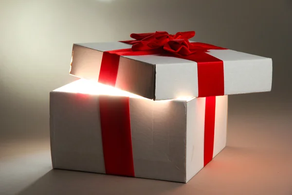 Gift box with bright light on it on grey background — Stock Photo, Image
