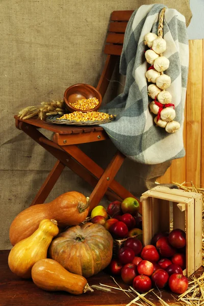 Apples in crate and pumpkins on wooden board and chair on sackcloth background — Stock Photo, Image