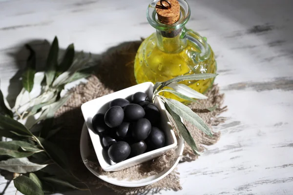 Оливковое масло и оливки в миске на мешковине на деревянном столе — стоковое фото
