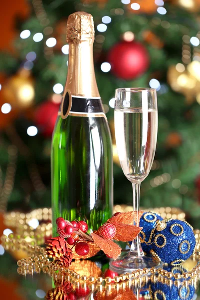 Бутылка шампанского со стеклом и рождественскими шарами на фоне елки — стоковое фото
