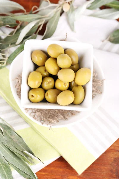 Olive in ciotola con ramo su tovagliolo su tavola di legno — Foto Stock