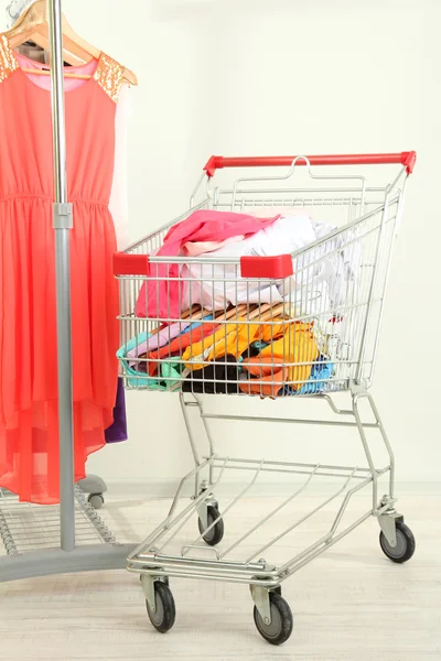 Carro de compras con ropa, sobre fondo gris — Foto de Stock