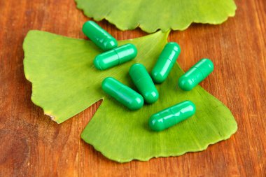 Ginkgo biloba leaves and pills on wooden background clipart