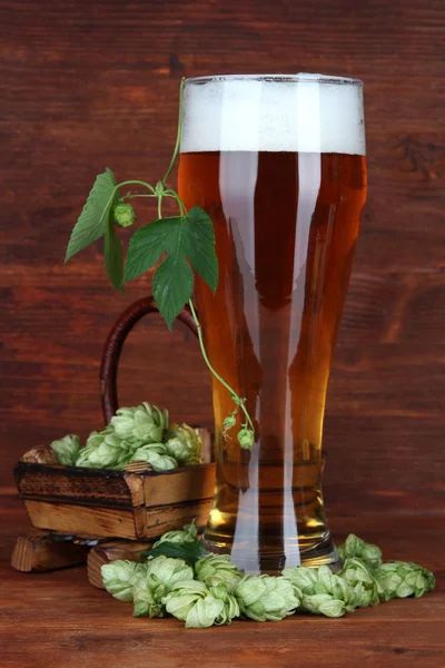 Vaso de cerveza y lúpulo, sobre mesa de madera — Foto de Stock