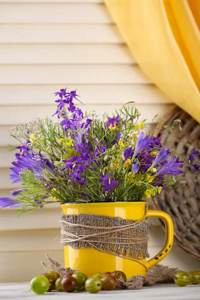 Beautiful bouquet of wildflowers in cup and berries on wooden table — Stock Photo, Image