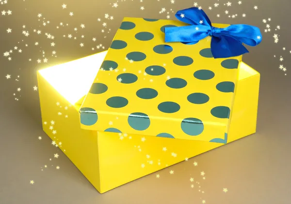 Gift box with bright light on it on grey background — Stock Photo, Image