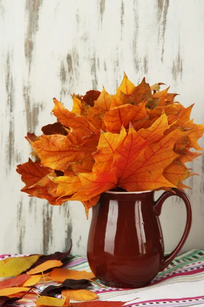 Красивые осенние листья в кувшине на столе на деревянном фоне — стоковое фото