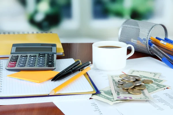 Bürobedarf mit Geld und einer Tasse Kaffee auf einem Tisch vor hellem Hintergrund — Stockfoto