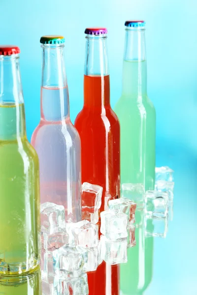 Bebidas en botellas de vidrio con hielo sobre fondo azul — Foto de Stock