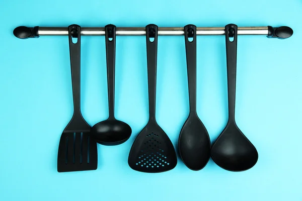 Plastic kitchen utensils on silver hooks on blue background — Stock Photo, Image