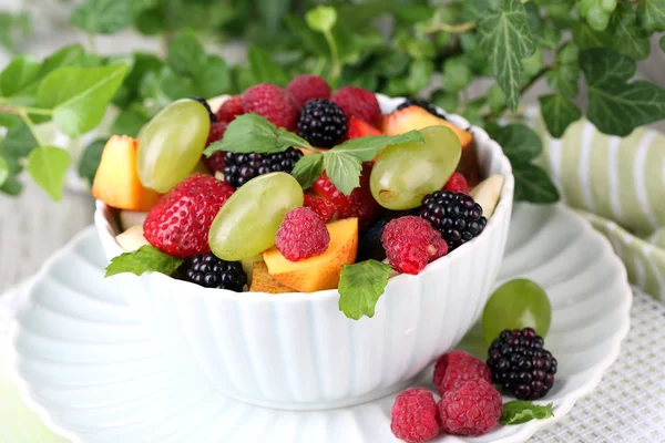 Fruit salad in bowl, on wooden table, on bright background — Stock Photo, Image