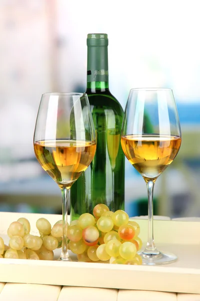 Ripe grapes, bottle and glasses of wine on tray, on bright background — Stock Photo, Image