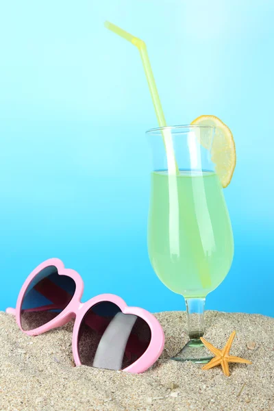 Beach cocktail in sand on blue background — Stock Photo, Image