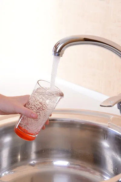 Hand holding glass of water poured from kitchen faucet — Stock Photo, Image