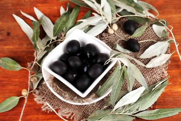 Olive in ciotola con ramo su sacco su tavolo di legno — Foto Stock
