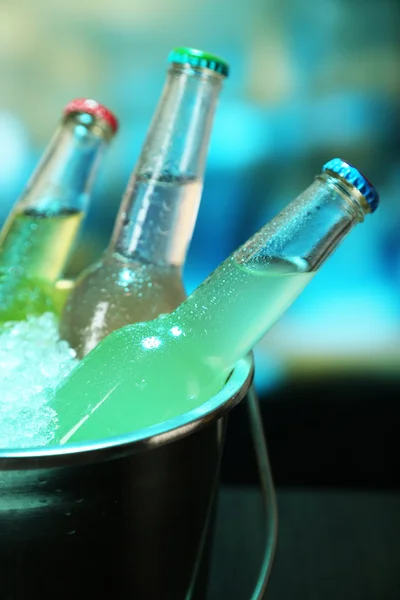 Bebidas engarrafadas em balde de gelo na mesa em fundo brilhante — Fotografia de Stock