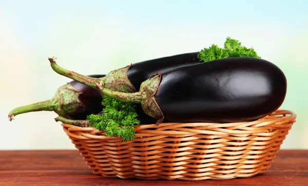 Fresh eggplants in wicker basket on table on wooden background — Stock Photo, Image